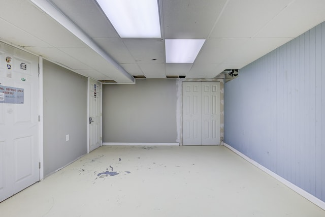 interior space with a drop ceiling, baseboards, and wood walls