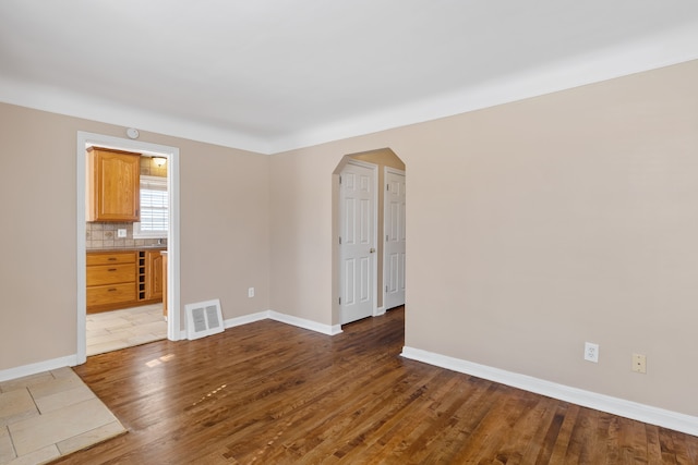 spare room with visible vents, arched walkways, dark wood-style flooring, and baseboards