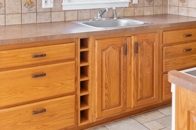 kitchen featuring a sink, backsplash, brown cabinetry, and light tile patterned floors