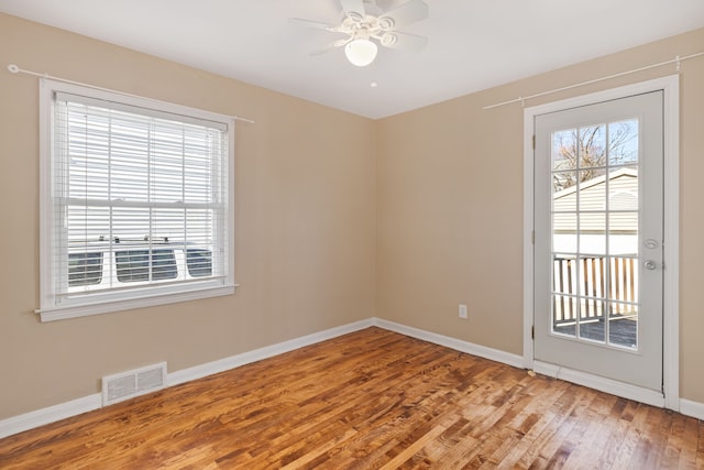 empty room with a ceiling fan, wood finished floors, visible vents, and baseboards