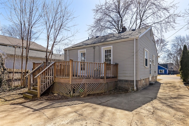 back of house featuring driveway, a deck, a chimney, and a shingled roof