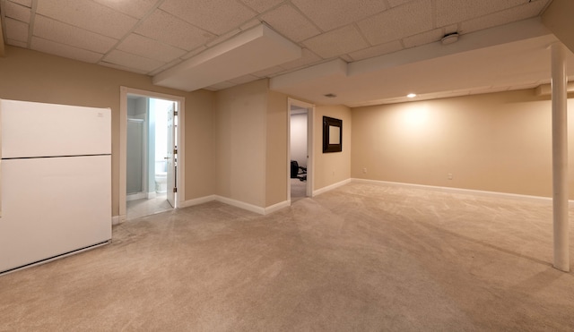 basement with light carpet, a drop ceiling, freestanding refrigerator, and baseboards