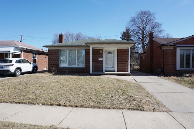 bungalow with a front yard, brick siding, and a chimney