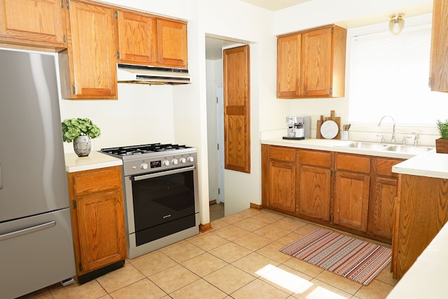 kitchen featuring under cabinet range hood, a sink, stainless steel appliances, brown cabinetry, and light countertops