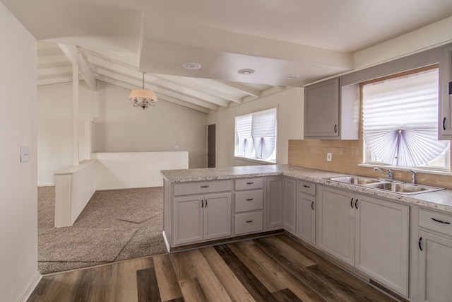 kitchen with vaulted ceiling with beams, dark wood-type flooring, light countertops, a peninsula, and a sink