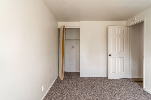 unfurnished bedroom with baseboards, dark colored carpet, and a closet