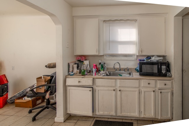 kitchen featuring black microwave, light tile patterned floors, light countertops, arched walkways, and a sink