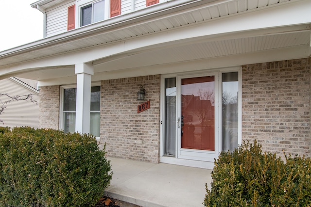 doorway to property featuring covered porch and brick siding