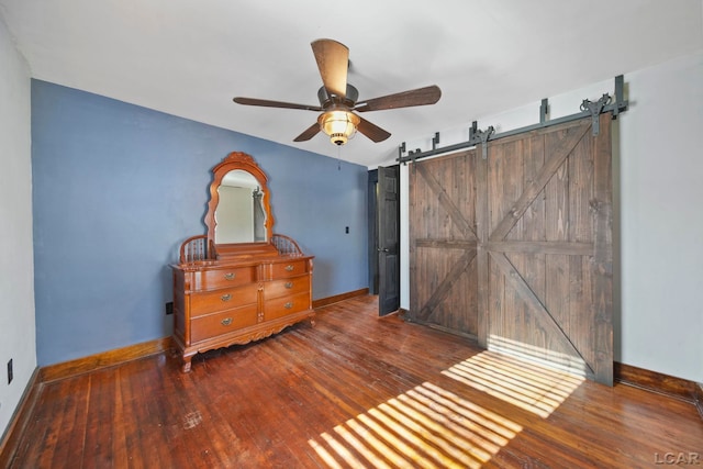 bedroom featuring ceiling fan, baseboards, a barn door, and hardwood / wood-style flooring