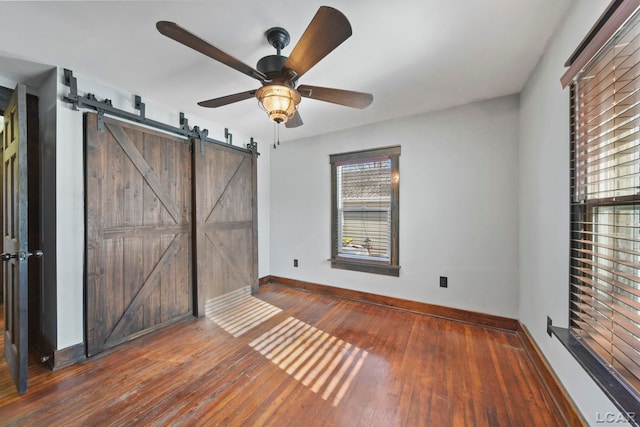 unfurnished bedroom featuring a barn door, a ceiling fan, baseboards, and wood-type flooring