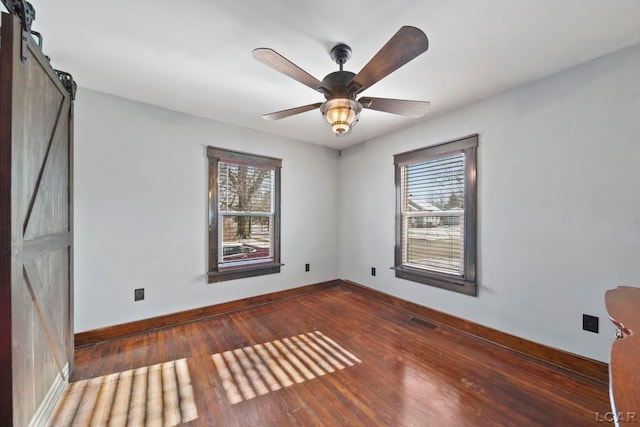 spare room with a barn door, baseboards, visible vents, and wood finished floors