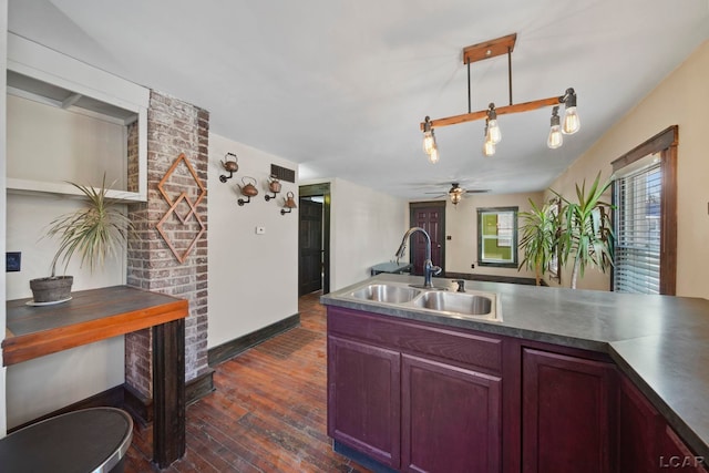 kitchen featuring ceiling fan, hanging light fixtures, dark wood-type flooring, a sink, and dark countertops