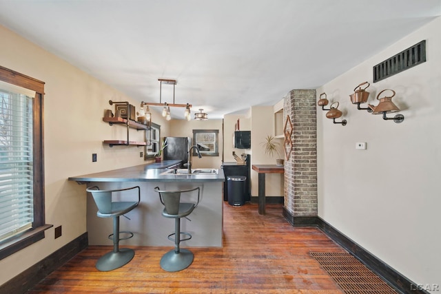 kitchen featuring a peninsula, visible vents, dark wood-style flooring, and a sink