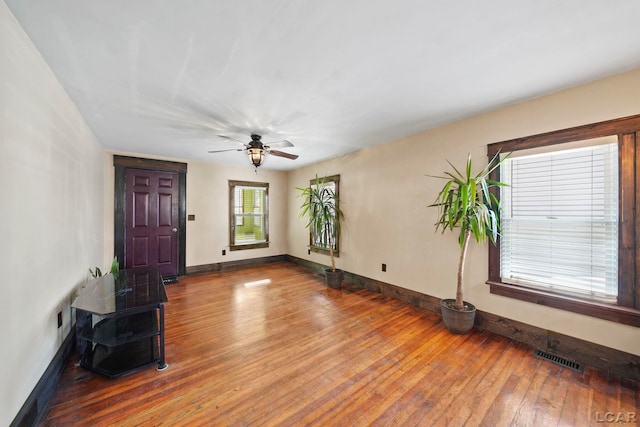 unfurnished living room with ceiling fan, visible vents, baseboards, and hardwood / wood-style floors