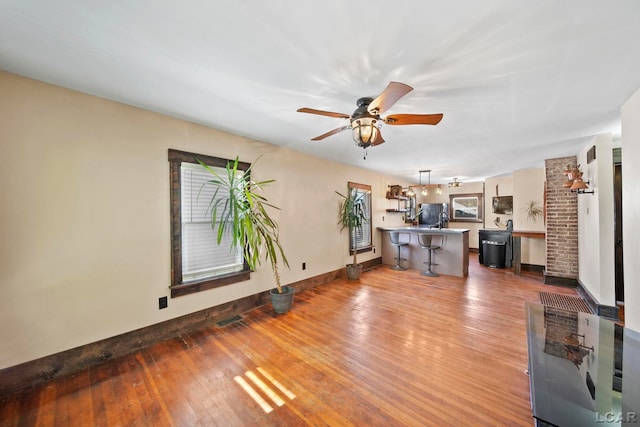 unfurnished living room with visible vents, baseboards, a ceiling fan, and hardwood / wood-style flooring