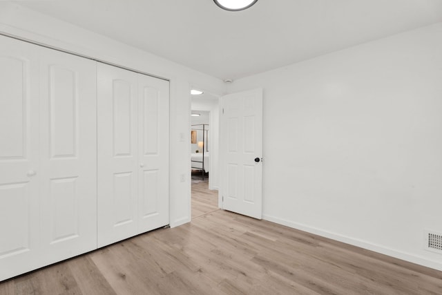 unfurnished bedroom with light wood-type flooring, baseboards, and a closet