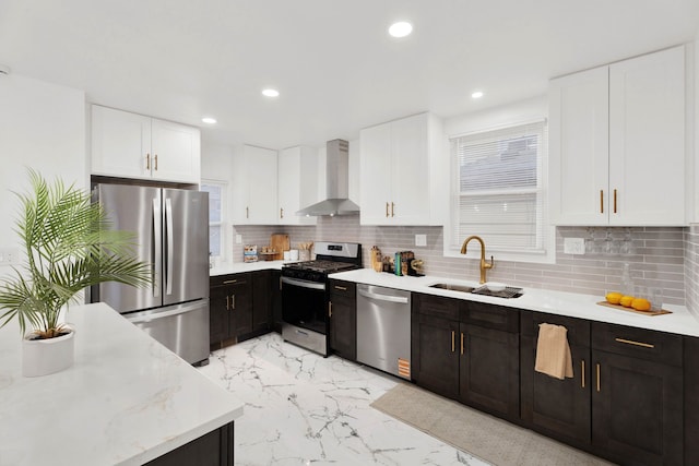 kitchen with a sink, marble finish floor, appliances with stainless steel finishes, wall chimney range hood, and tasteful backsplash