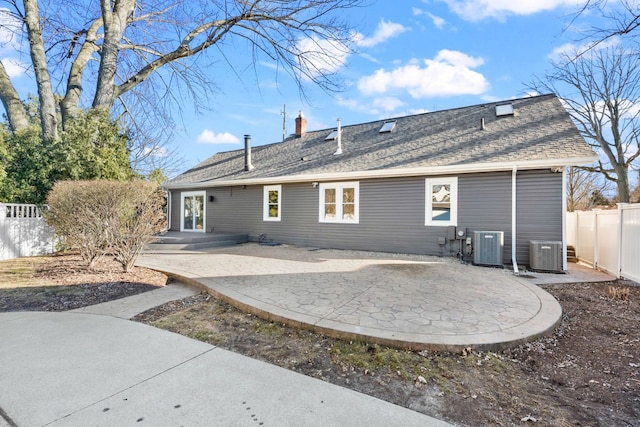 rear view of property with central air condition unit, fence, a shingled roof, and a patio area