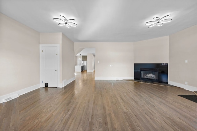 unfurnished living room featuring visible vents, baseboards, wood finished floors, and a fireplace