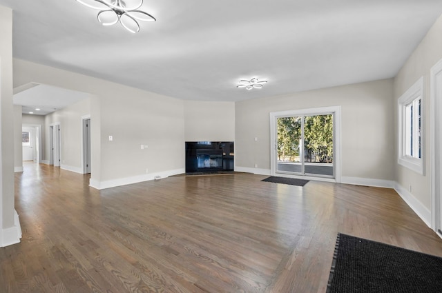 unfurnished living room featuring wood finished floors, baseboards, plenty of natural light, and a glass covered fireplace