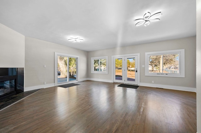 unfurnished living room featuring dark wood-style floors, a tile fireplace, french doors, and baseboards