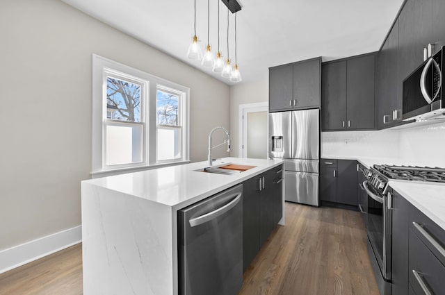 kitchen featuring dark wood-type flooring, a sink, stainless steel appliances, light countertops, and hanging light fixtures