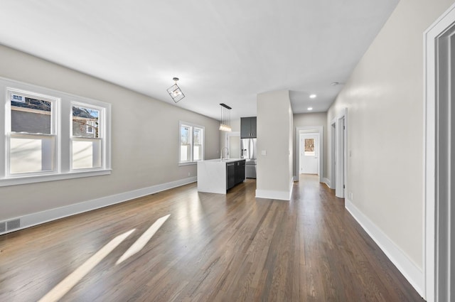 unfurnished living room with visible vents, a sink, baseboards, and dark wood-style flooring