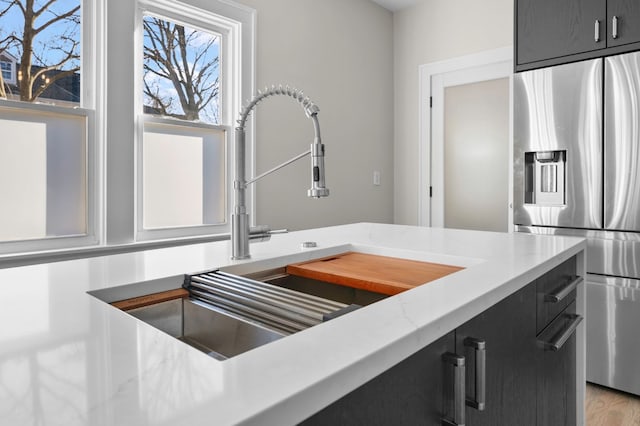 kitchen with dark cabinets, stainless steel refrigerator with ice dispenser, and a sink