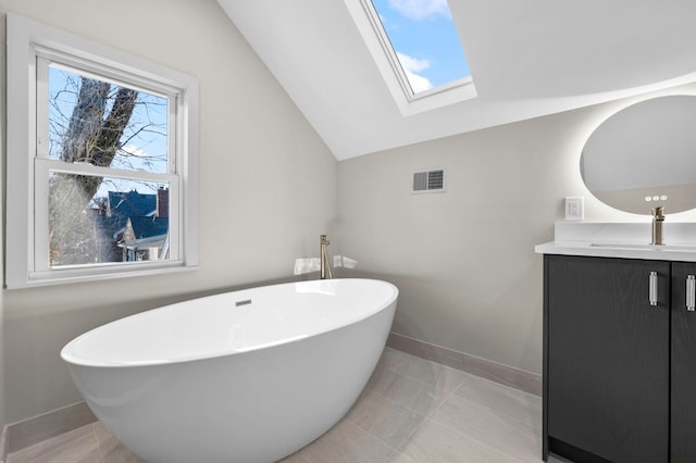 full bathroom with vanity, baseboards, visible vents, a freestanding tub, and lofted ceiling with skylight