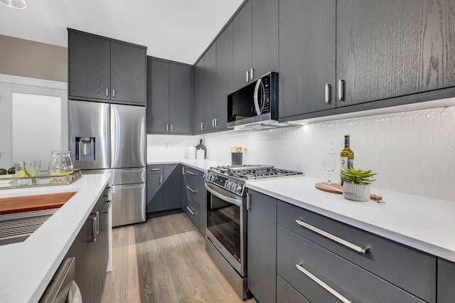 kitchen featuring light countertops, tasteful backsplash, gray cabinets, light wood finished floors, and appliances with stainless steel finishes