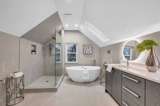 bathroom featuring vanity, a freestanding tub, a tile shower, vaulted ceiling with skylight, and visible vents