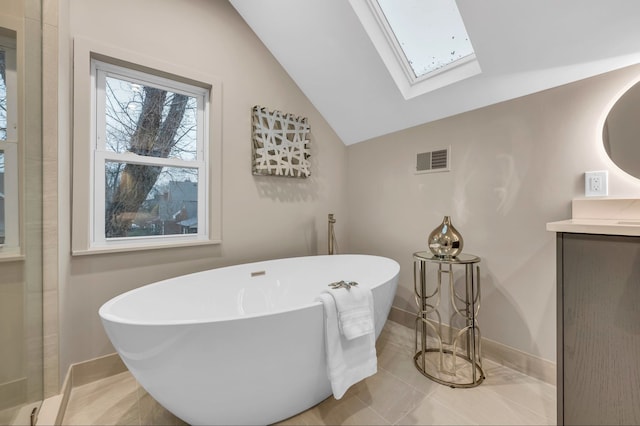 bathroom with vanity, a freestanding tub, lofted ceiling with skylight, baseboards, and visible vents