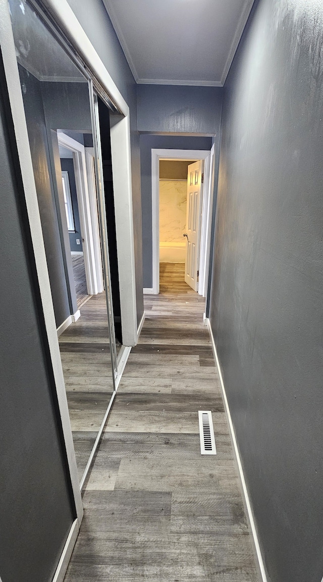 hall featuring visible vents, crown molding, baseboards, and wood finished floors