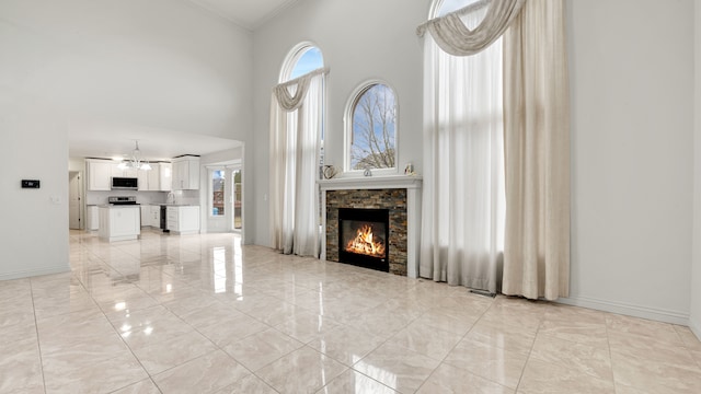 unfurnished living room featuring baseboards, a stone fireplace, a towering ceiling, crown molding, and marble finish floor