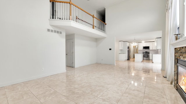 unfurnished living room with visible vents, a notable chandelier, a glass covered fireplace, baseboards, and a towering ceiling