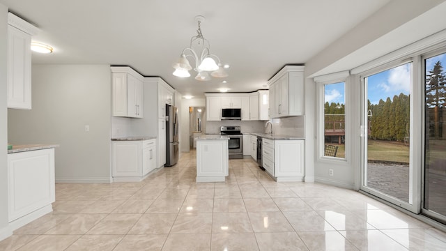 kitchen featuring a sink, white cabinetry, appliances with stainless steel finishes, an inviting chandelier, and light stone countertops