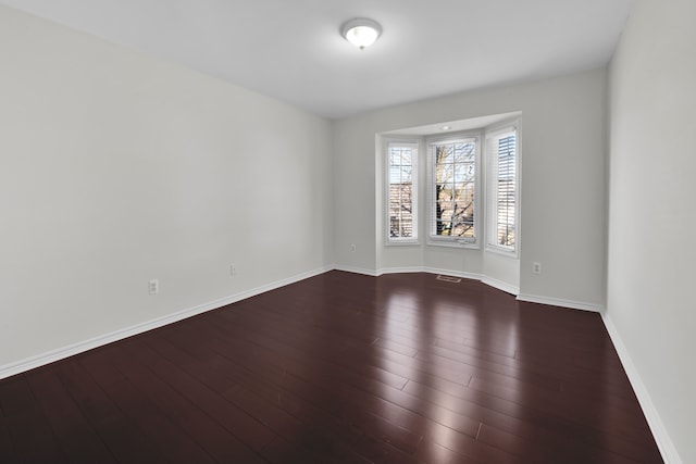 spare room featuring visible vents, baseboards, and dark wood finished floors