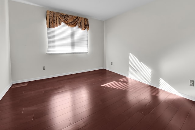 spare room featuring visible vents, dark wood-type flooring, and baseboards