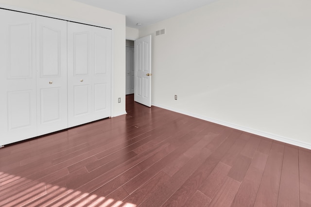 unfurnished bedroom with dark wood-style floors, visible vents, a closet, and baseboards