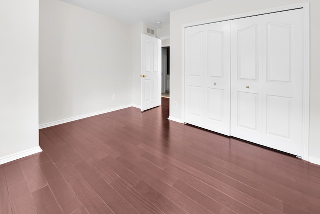 unfurnished bedroom featuring a closet, baseboards, visible vents, and dark wood finished floors