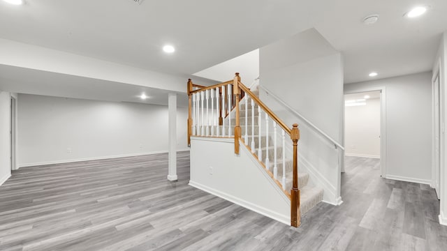 finished below grade area with recessed lighting, baseboards, wood finished floors, and stairs