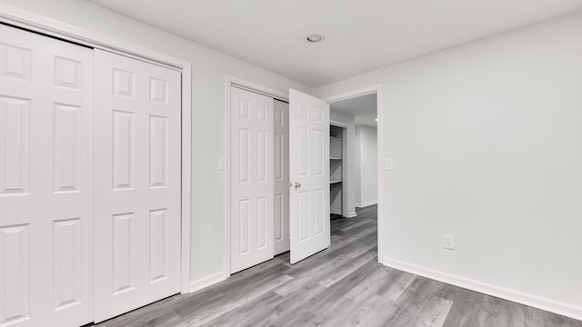 unfurnished bedroom with wood finished floors, baseboards, and two closets