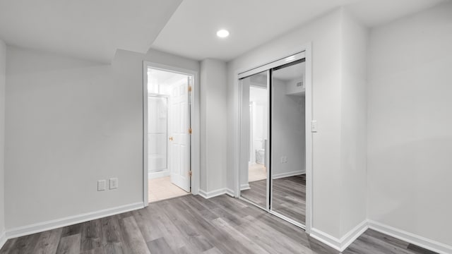 unfurnished bedroom with a closet, connected bathroom, baseboards, and wood finished floors