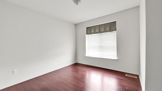 unfurnished room featuring visible vents, baseboards, and dark wood-style floors