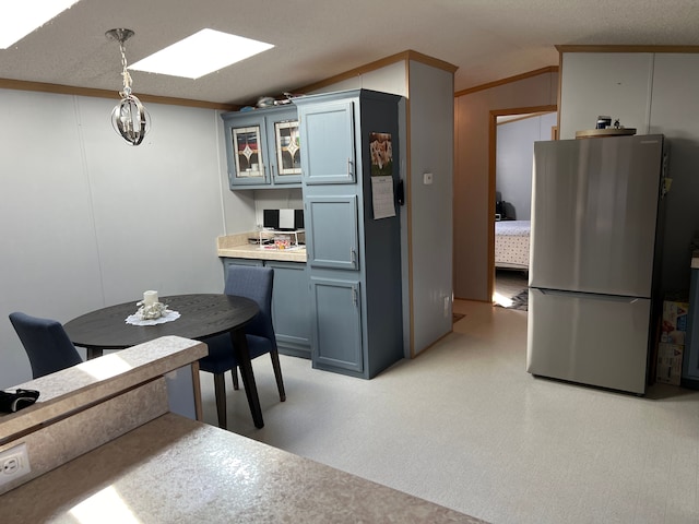 kitchen featuring glass insert cabinets, light floors, vaulted ceiling with skylight, freestanding refrigerator, and hanging light fixtures