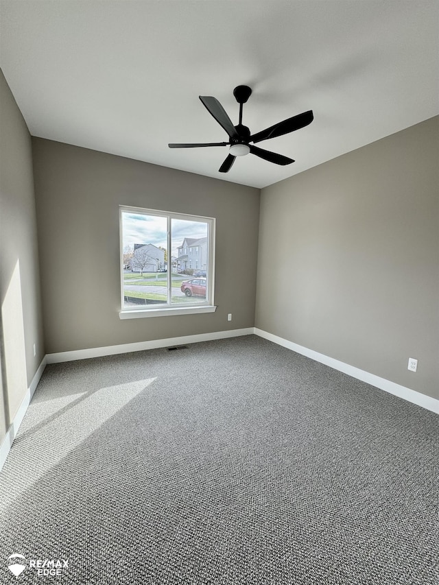 carpeted spare room with visible vents, baseboards, and ceiling fan