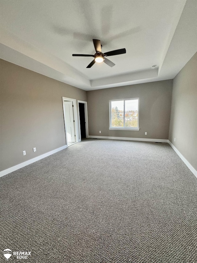 unfurnished room featuring ceiling fan, baseboards, a tray ceiling, and carpet floors