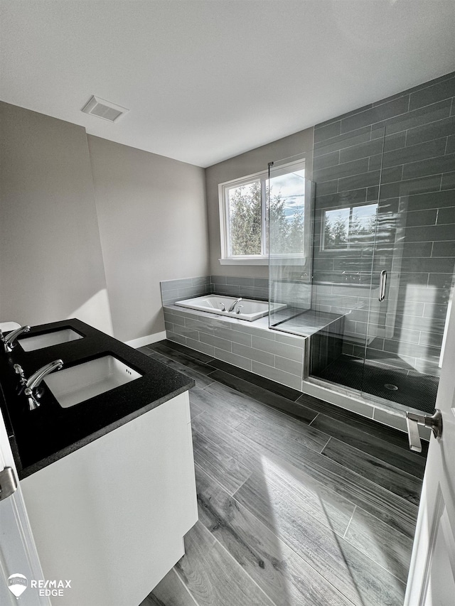 full bath with visible vents, double vanity, a stall shower, a sink, and a garden tub