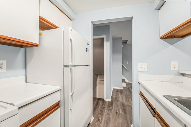 kitchen with light countertops, freestanding refrigerator, wood finished floors, white cabinetry, and a sink