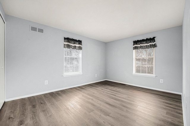 spare room featuring wood finished floors, a healthy amount of sunlight, visible vents, and baseboards